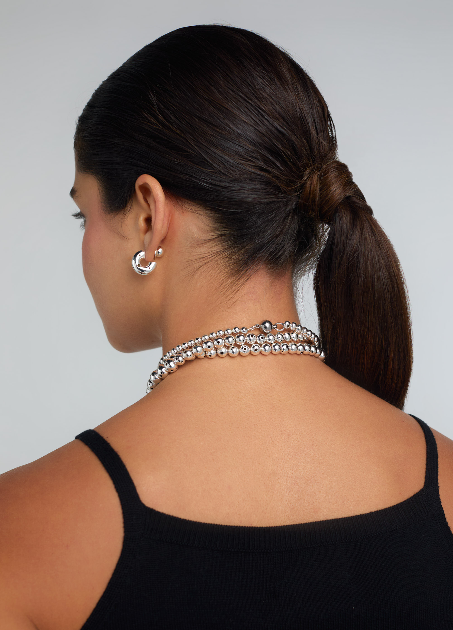 Back close up of a model wearing a silver beaded necklace twisted three times and showing the clasp the necklace has in the back.